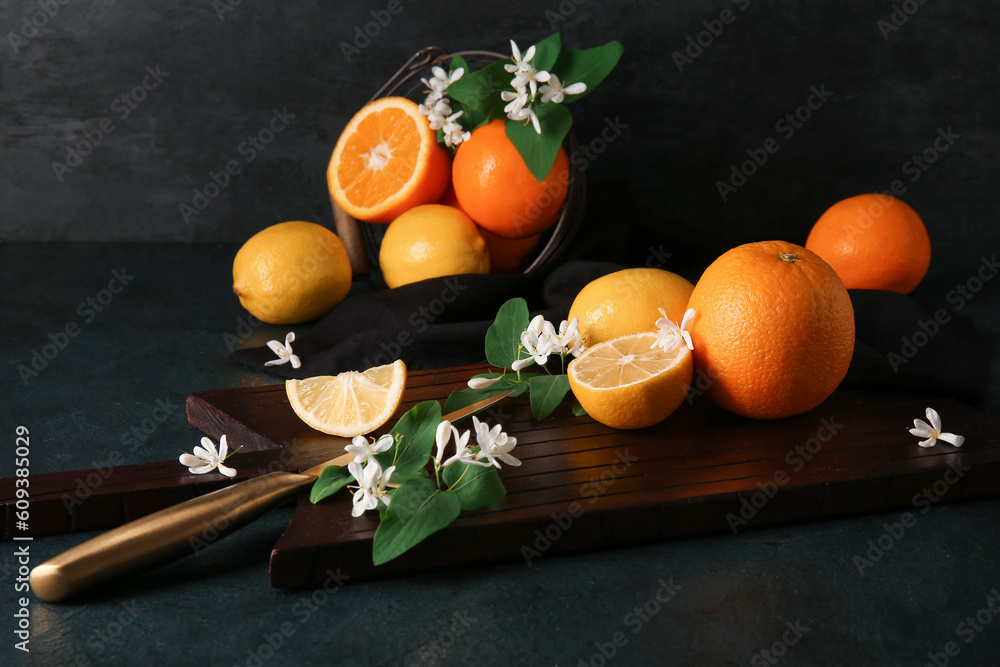 Board of lemons and oranges with blooming branches on black background