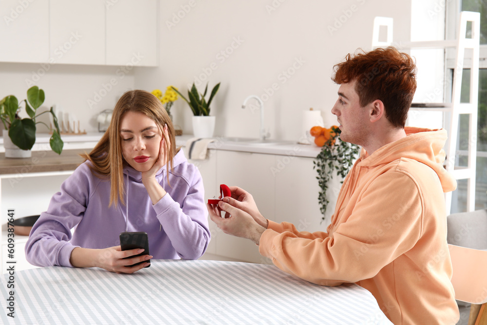 Young man proposing to his girlfriend using mobile phone in kitchen