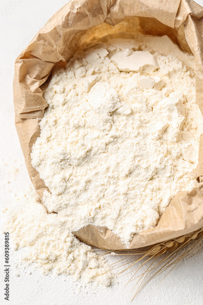 Paper bag with flour and wheat ear on white background