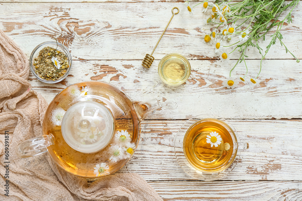 Cup of hot chamomile tea, teapot and honey on light wooden background