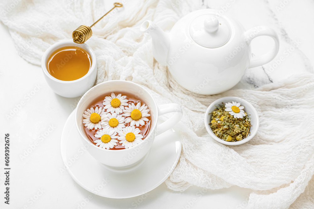 Cup of hot chamomile tea, teapot and honey on white marble background