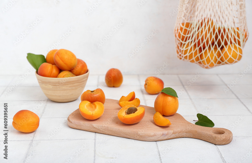 Board and bowl with fresh apricots on white tile table