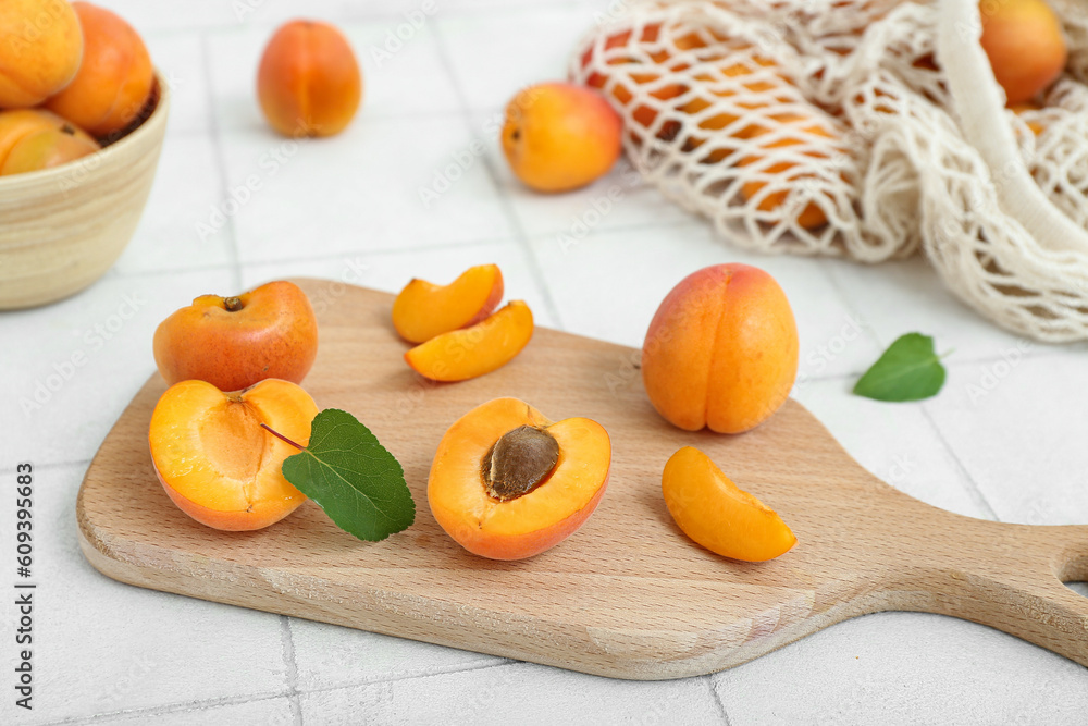 Board and bowl with fresh apricots on white tile table