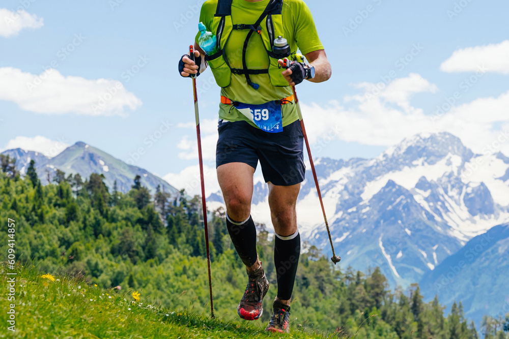 athlete runner running skyrunning race in background snowy mountain, trekking poles in hands and bac