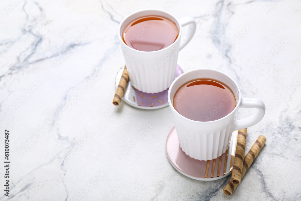 Drink coasters with cups of tea and wafer rolls on white marble table