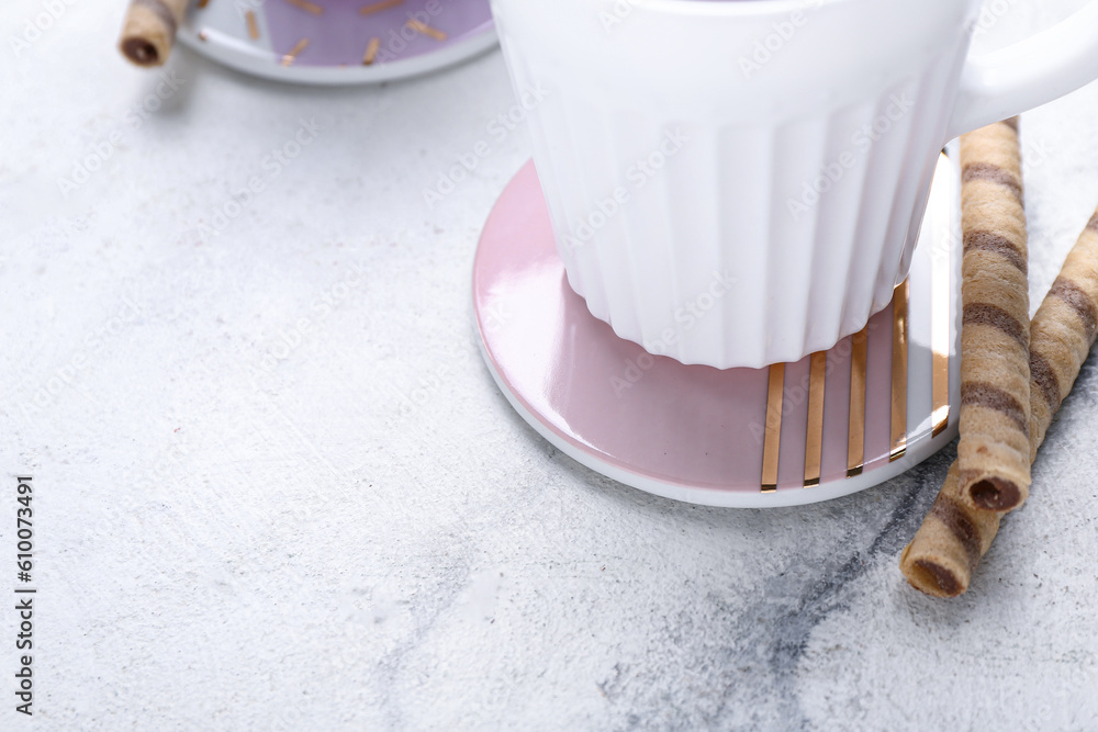 Drink coaster with cup and wafer rolls on white marble table, closeup