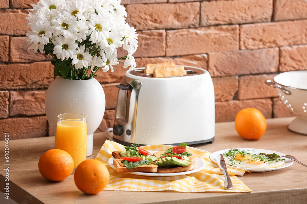 Modern toaster with crispy bread slices, toasts, fried eggs and glass of orange juice on table