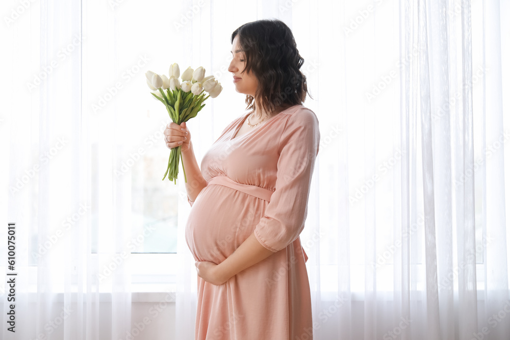 Young pregnant woman with tulips near window at home