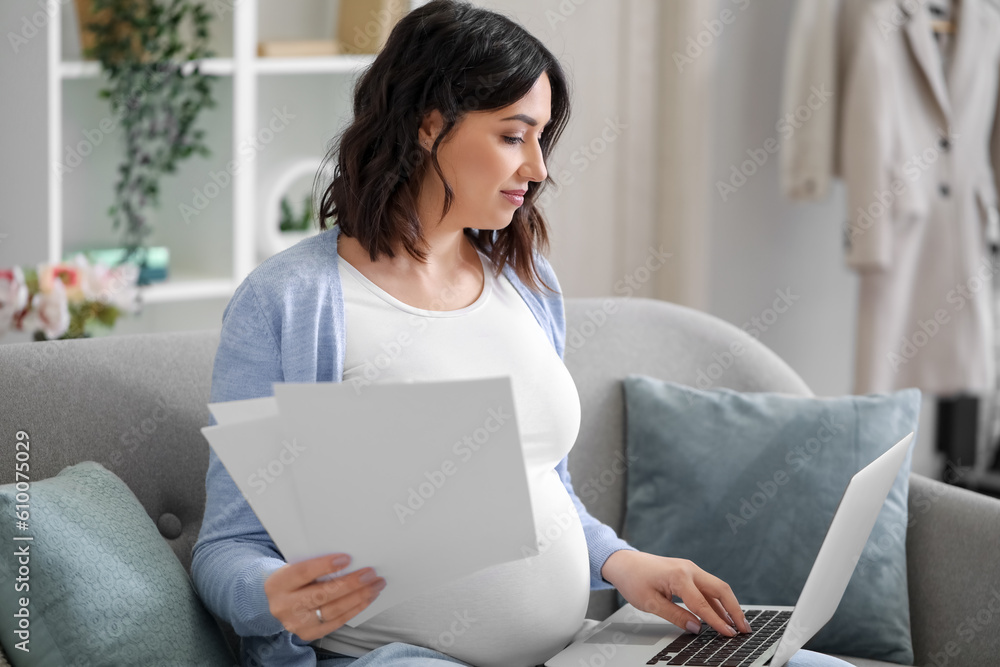 Young pregnant woman working with documents and laptop at home