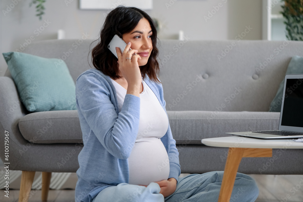 Working pregnant woman talking by mobile phone at home