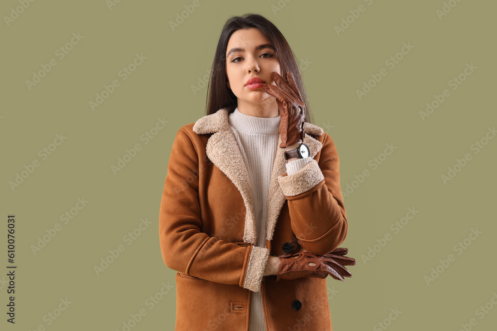 Stylish young woman in leather gloves on green background