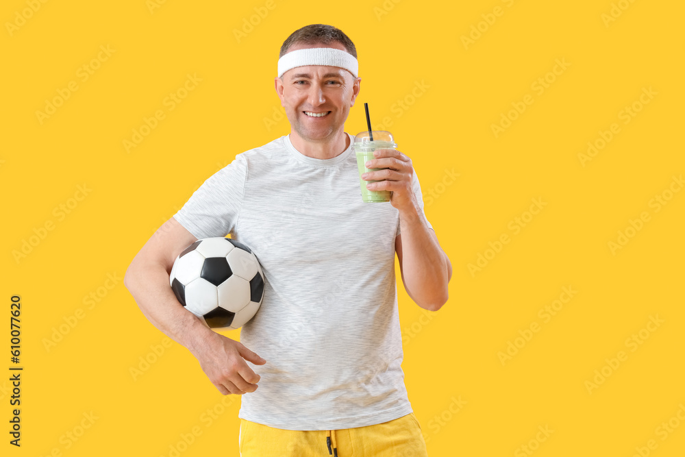 Sporty mature man with glass of vegetable smoothie and soccer ball on yellow background