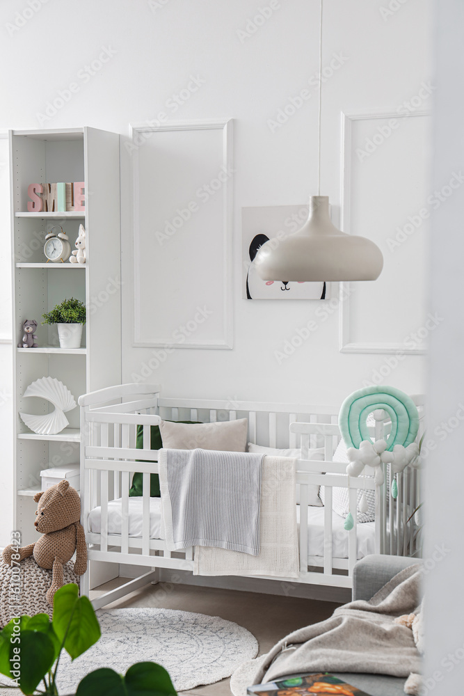 Stylish interior of childrens room in white tones with baby bed and shelving unit