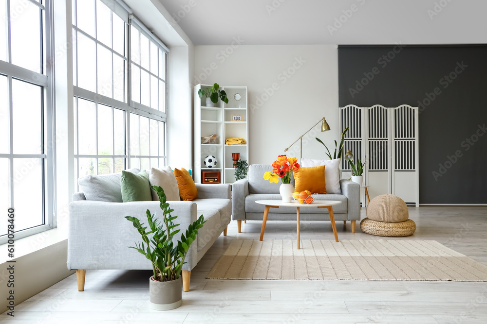 Interior of bright living room with sofas and tulip flowers on coffee table near big window