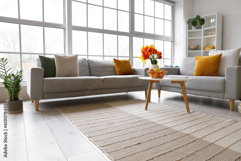 Interior of bright living room with sofas and tulip flowers on coffee table near big window