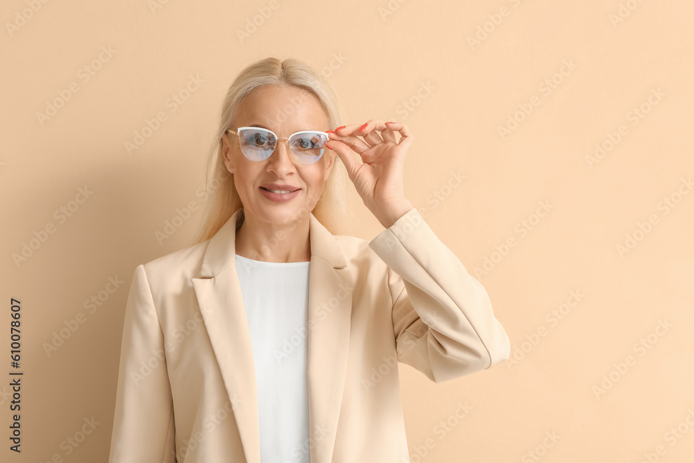 Mature blonde woman in eyeglasses on beige background