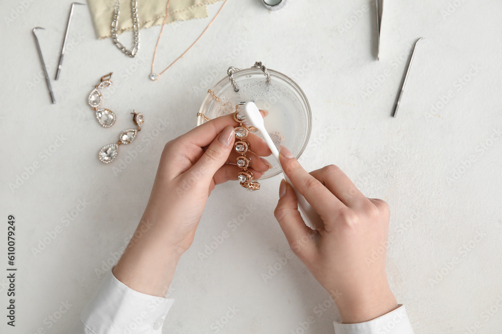 Woman cleaning beautiful bracelet with toothbrush on light background, closeup