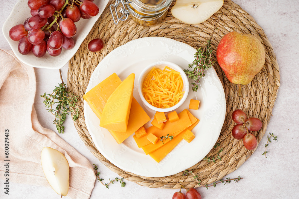 Plate with tasty cheddar cheese, grapes and olives on light background