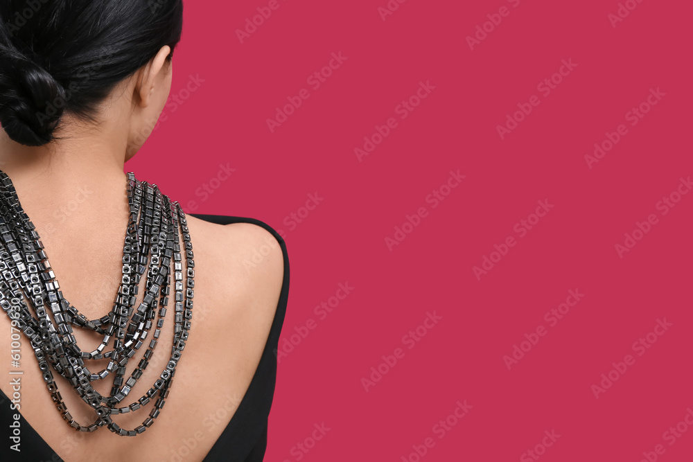 Beautiful young woman wearing massive necklace near red wall, back view