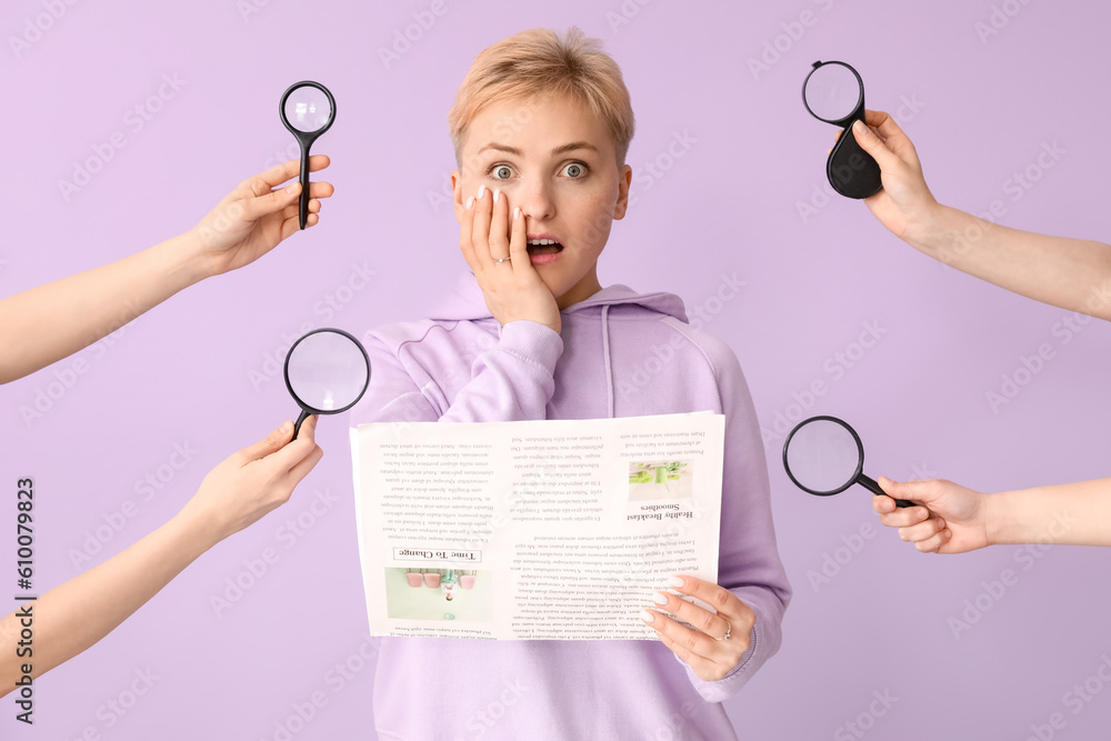 Young woman holding newspaper and female hands with magnifiers on lilac background