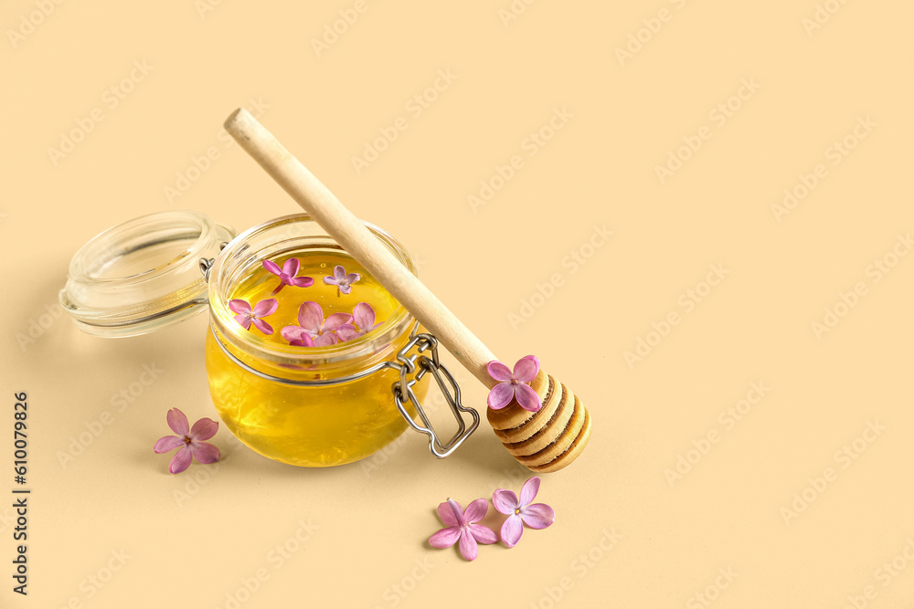 Jar of honey and lilac flowers on beige background