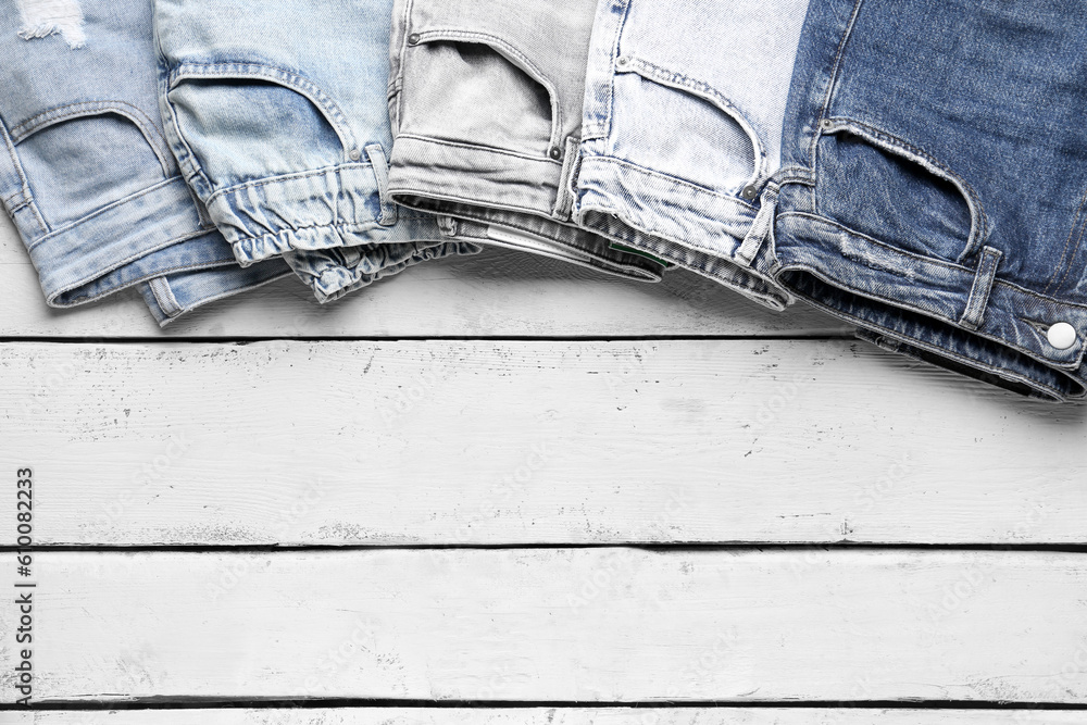 Different stylish denim jeans on wooden background, closeup