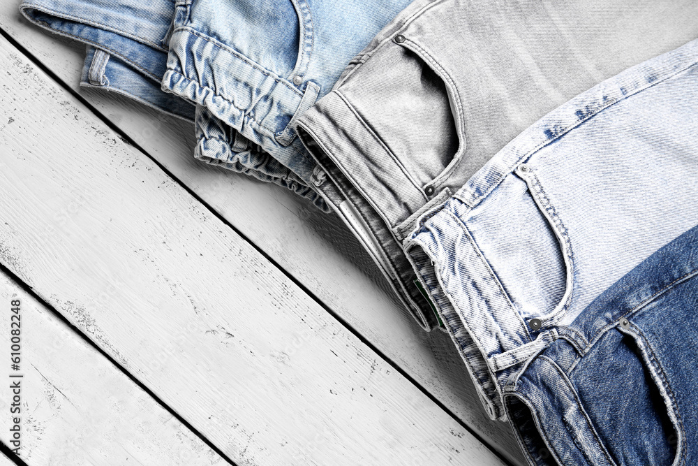 Different stylish denim jeans on wooden background, closeup