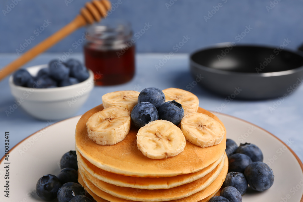 Plate with tasty pancakes, banana and blueberry on blue background, closeup