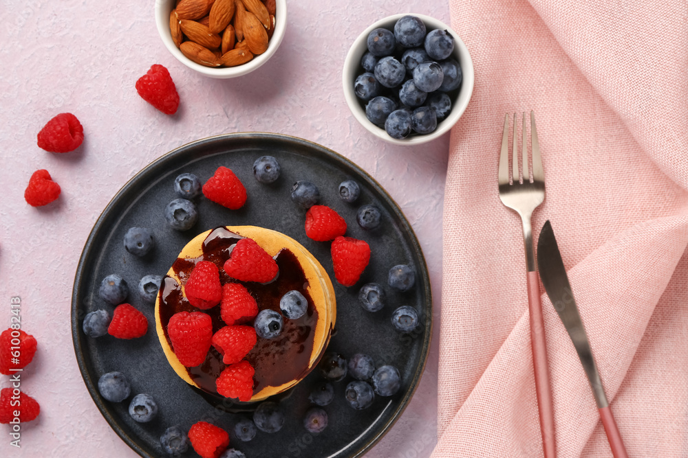 Plate with sweet pancakes, berries and nuts on pink background