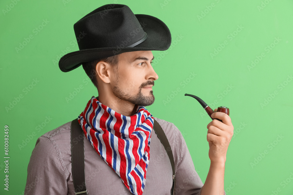 Handsome cowboy with smoking pipe on green background, closeup