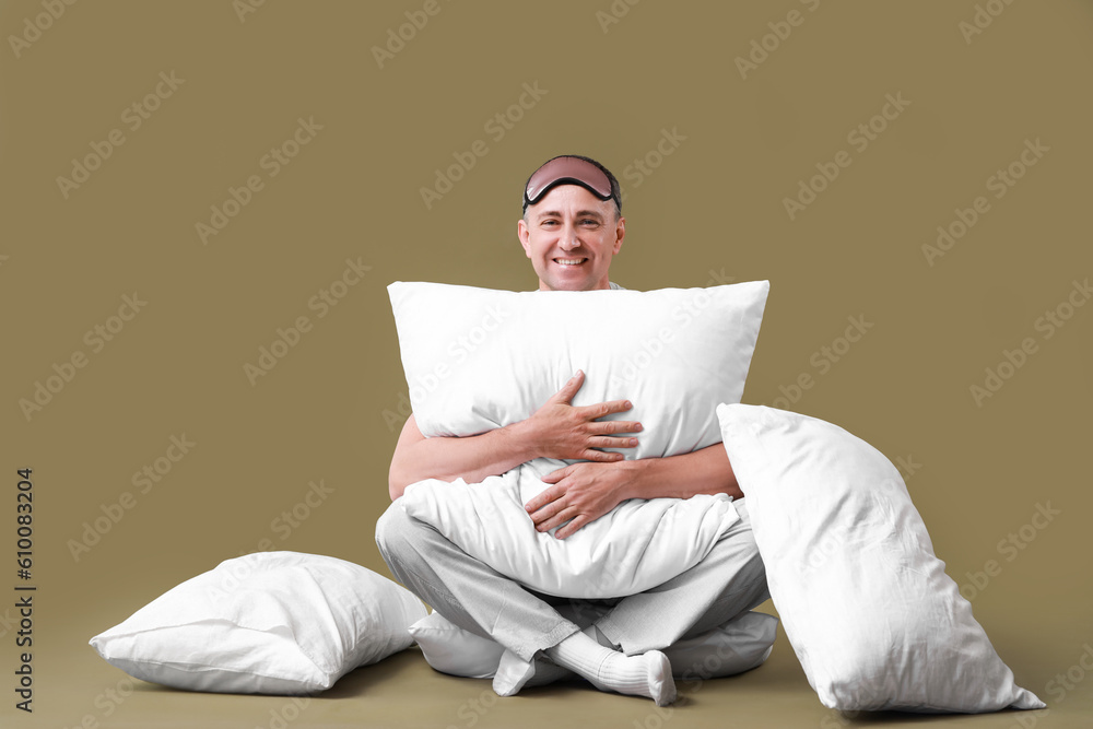 Mature man with soft pillows sitting on green background