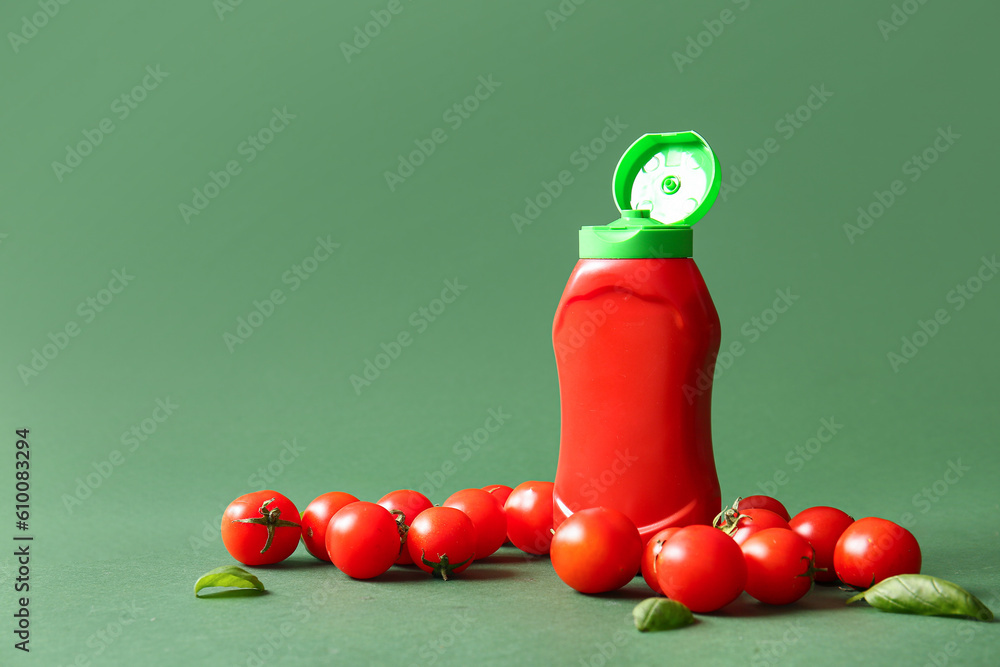 Bottle of ketchup and tomatoes on green background