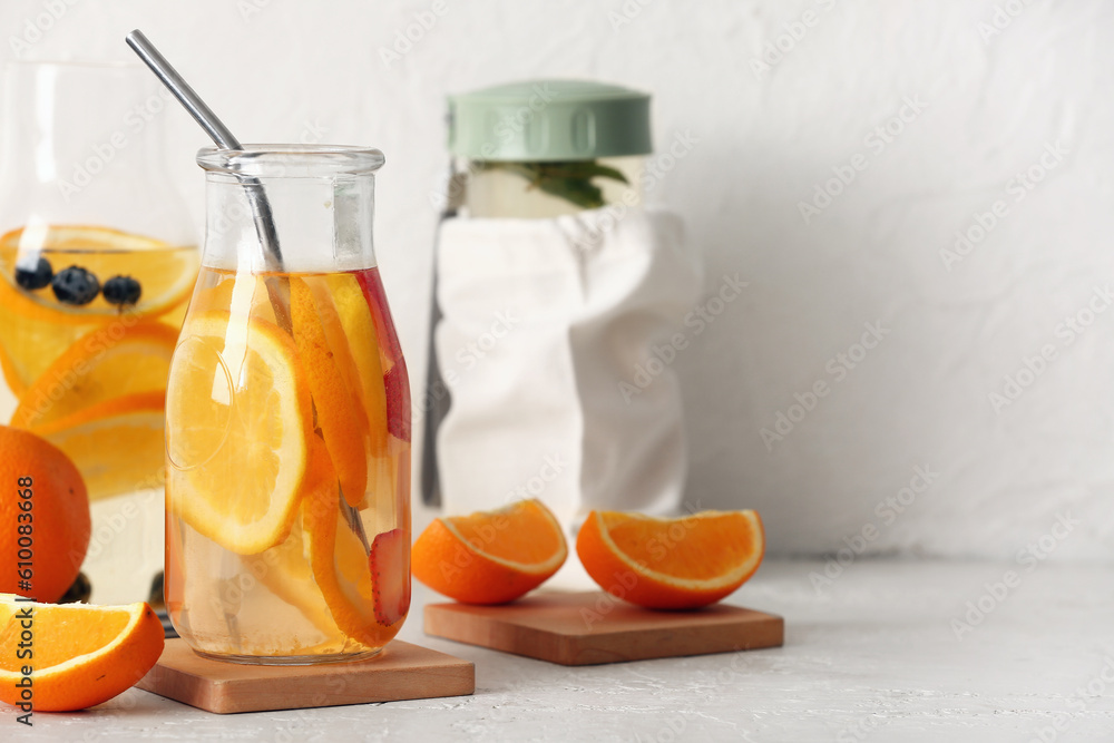 Bottles of infused water with orange slices on white table