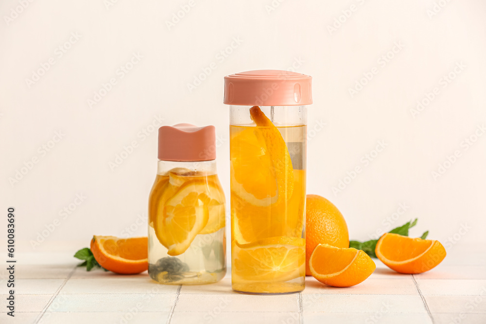 Sports bottles of infused water with orange slices on white tile table