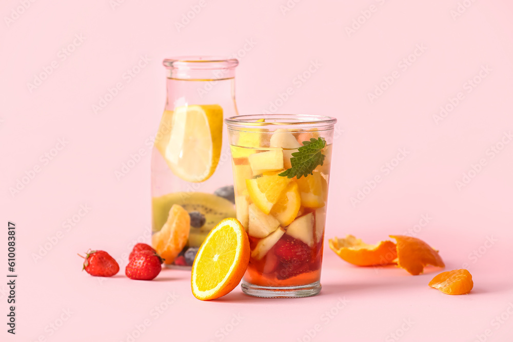 Glass and bottle of infused water with different sliced fruits on pink background