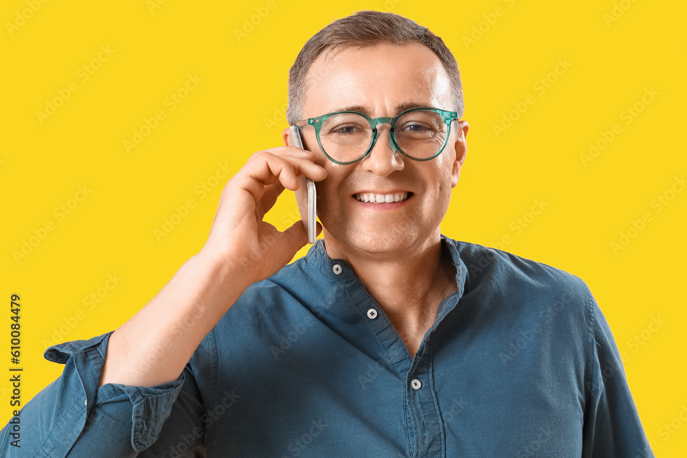 Mature man in eyeglasses talking by mobile phone on yellow background