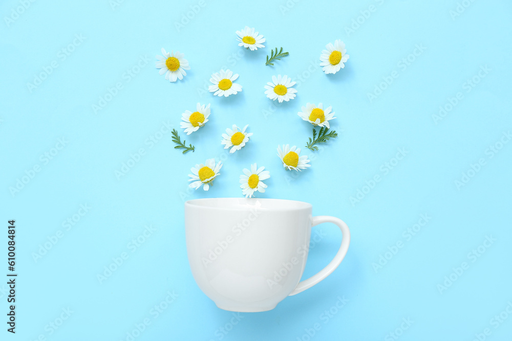 Cup with chamomile flowers on blue background