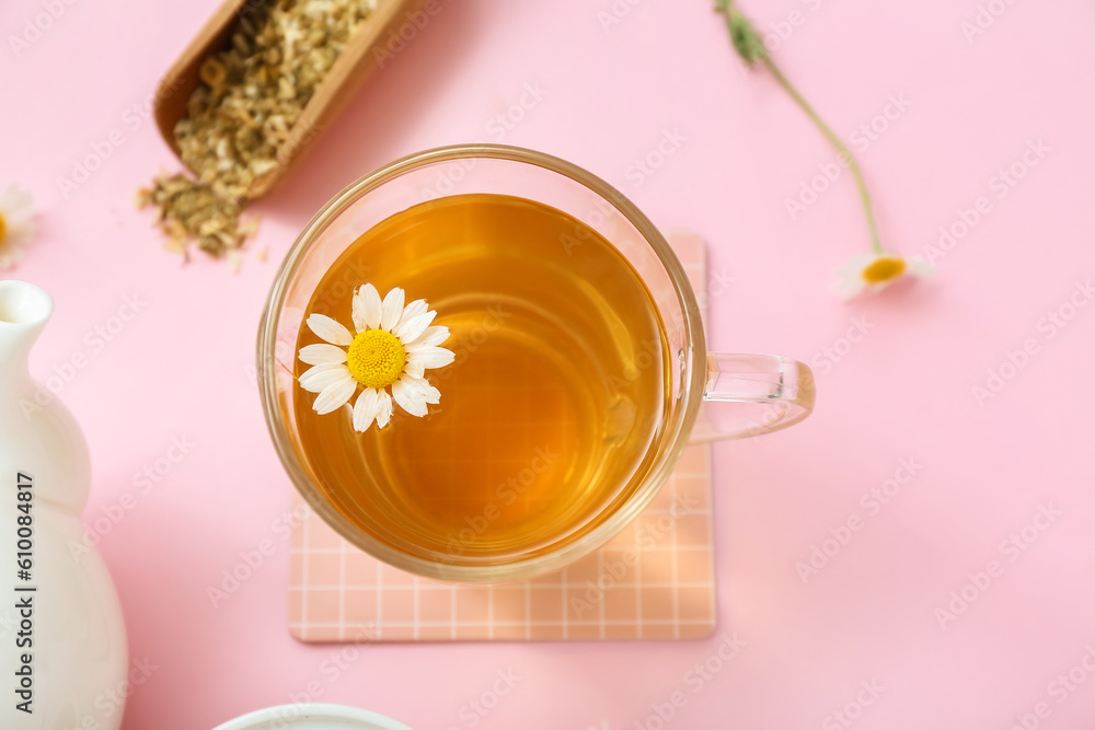 Teapot and cup of hot chamomile tea on pink background