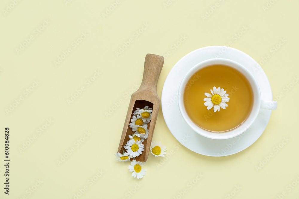 Cup of hot chamomile tea with scoop on pale yellow background