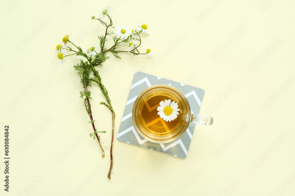 Cup of hot chamomile tea with flowers on pale yellow background