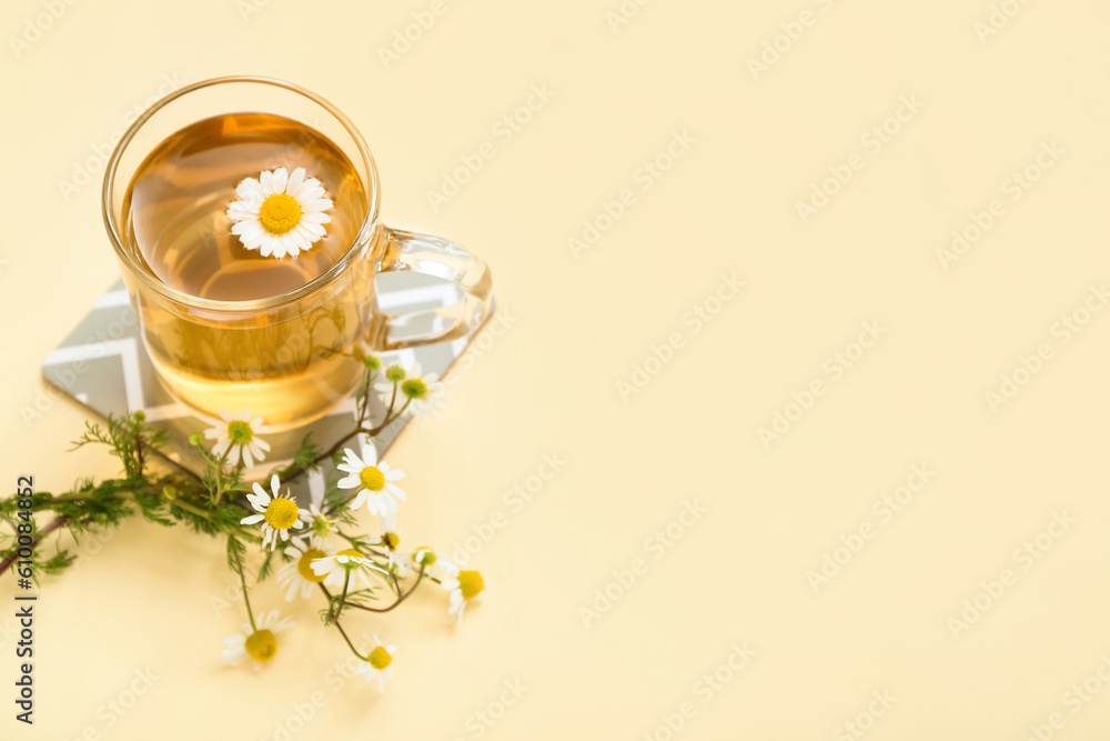 Cup of hot chamomile tea with flowers on pale yellow background