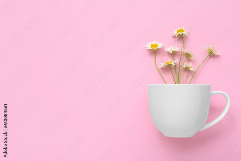 Cup with chamomile flowers on pink background