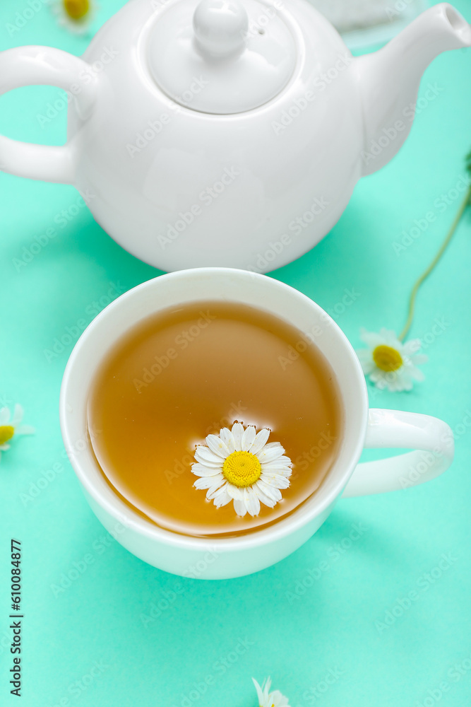 Teapot and cup of hot chamomile tea on turquoise background