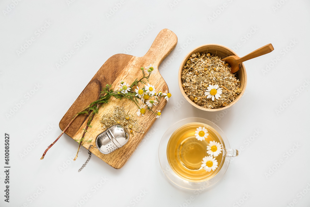 Cup of hot tea and bowl with dried chamomile on white background