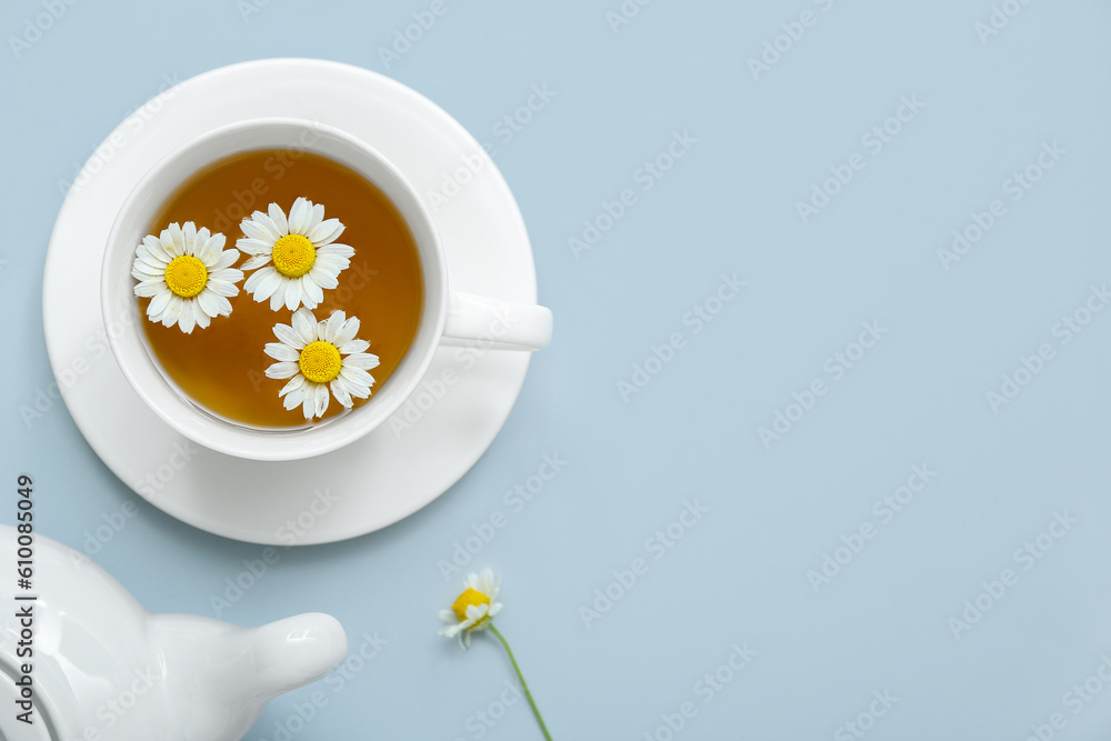 Teapot and cup of hot chamomile tea on pale blue background