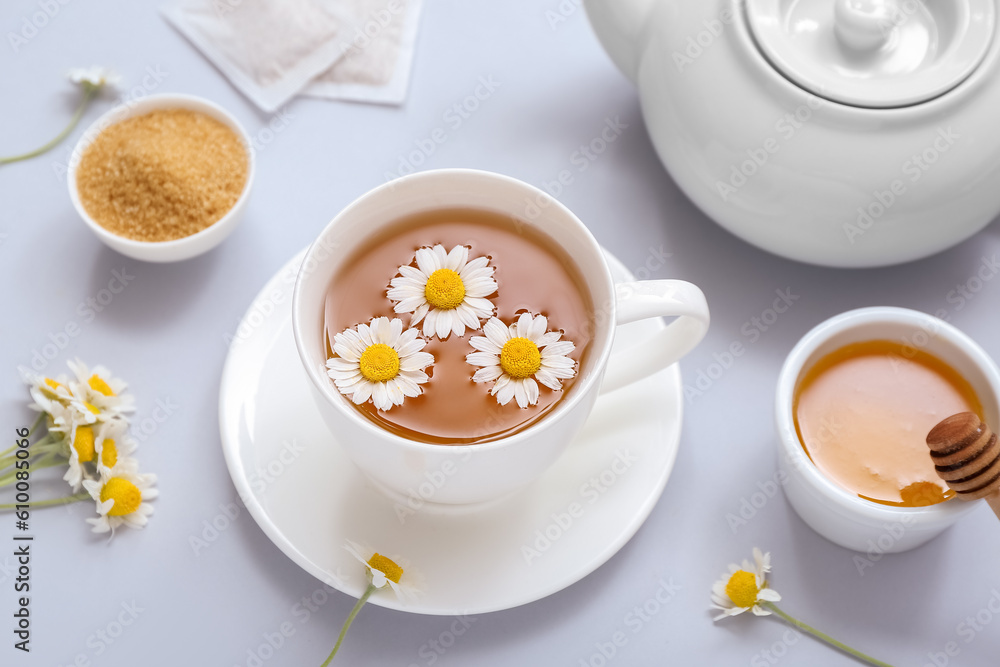 Teapot and cup of hot chamomile tea with honey on white background