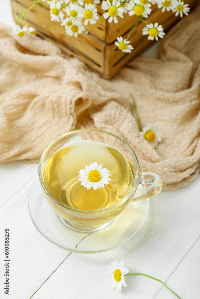 Cup of hot chamomile tea and box with flowers on white wooden background