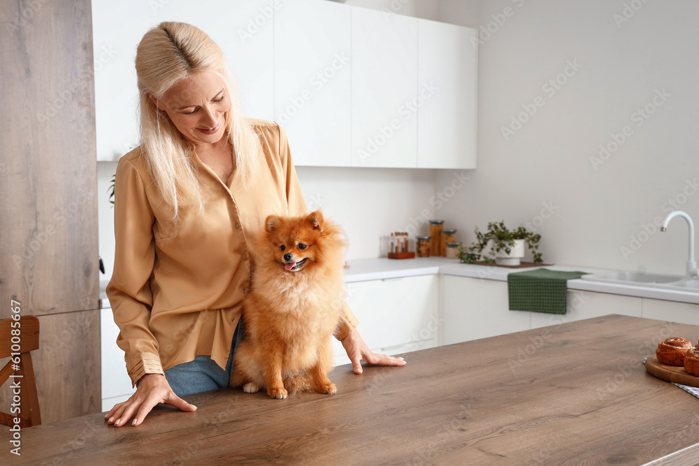 Mature woman with Pomeranian dog at table in kitchen