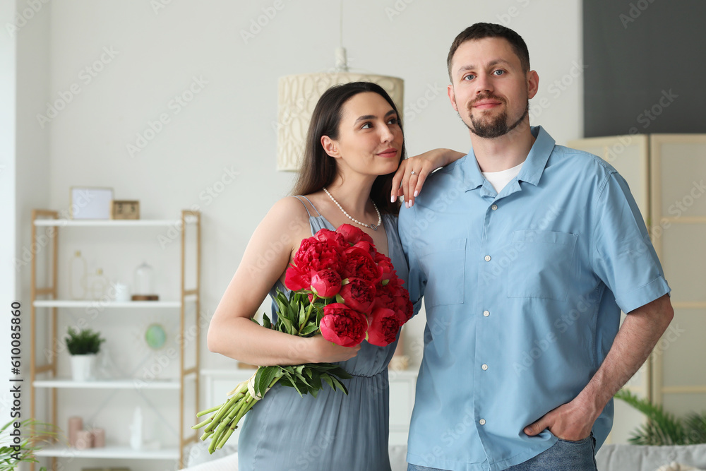 Happy engaged couple with flowers hugging at home