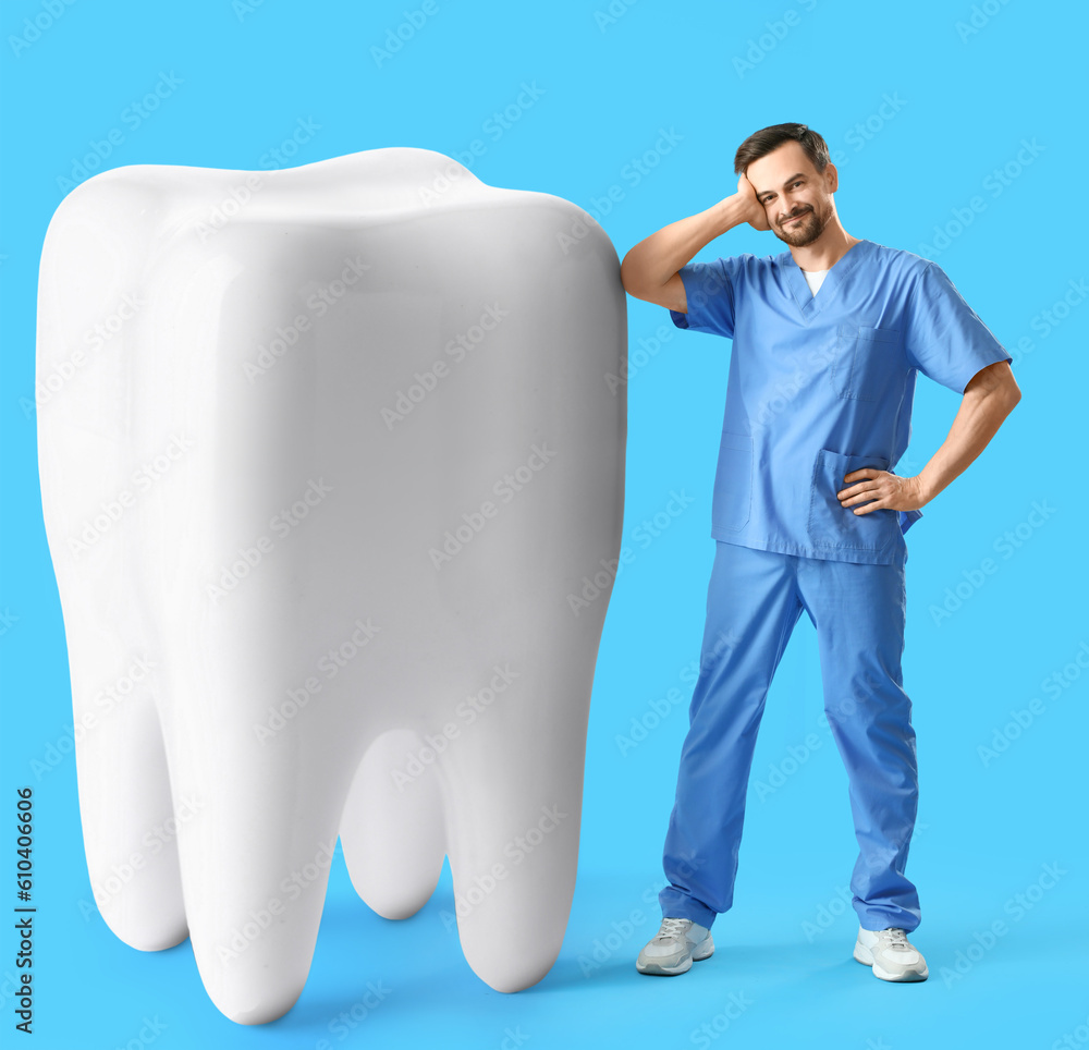 Male dentist with big tooth on light blue background